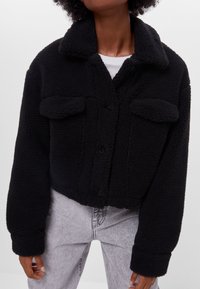 Czarna krótka kurtka z fakturowanego polaru, z kołnierzykiem, dwoma przednimi kieszeniami i zapięciem na guziki.