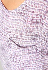 Lila mönstrad tyg med en geometrisk design som har en ficka. Materialet verkar lätt och mjukt med en subtil textur.