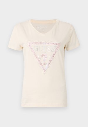 T-shirt in cotone beige a maniche corte con scollatura a V e un logo a triangolo rosa glitterato con la scritta "GUESS" e dettagli decorativi.