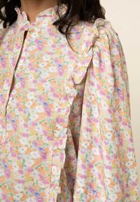 Blumenbluse mit Rüschensaum, in einer pastellfarbenen Farbpalette aus Orange, Pink und Weiß. Hergestellt aus weichem Stoff mit einem Knopfkragen.