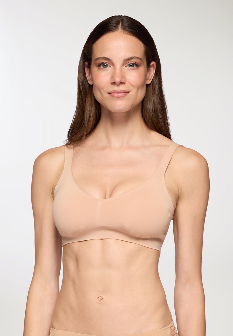 Senza ferretto, reggiseno wireless in nude con design senza cuciture, spalline larghe e texture morbida. Presenta un delicato scollo a V e una leggera sagomatura.