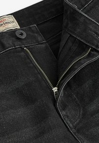 Jeans din denim negru cu fermoar, având accesorii metalice, cusături tonale și un eticheta de marcă pe talie. Design slim fit.