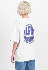 Biele oversized tričko vyrobené z bavlny s fialovým grafickým motívom na chrbte, na ktorom je nápis "ALPHA INDUSTRIES" a "SINCE 1959."