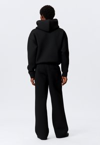 Schwarzer Hoodie und passende Hose aus dickem Stoff. Verfügt über eine Kapuze, lockere Passform und eine Gesäßtasche an der Hose. Einfaches Design.