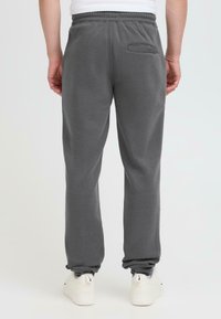 Grå joggebukser med snøring i livet, sidelomme og smalnende cuff, laget av myk stoff med en glatt tekstur.