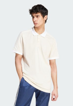 Cream-colored polo shirt with a white collar, three buttons, and short sleeves featuring white stripes along the shoulders. Subtle logo detail.