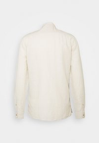 Camisa de manga larga beige claro, hecha de tela texturizada, con dobladillo redondeado y puños abotonados, y un diseño de cuello sencillo.