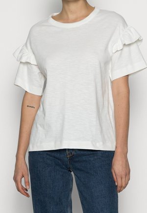 Valkoinen puuvillainen T-paita, jossa on lyhyet röyhelöhihat, pyöreä pääntie ja rento istuvuus. Yhdistetty tummansinisiin farkkuihin.