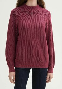 Sweter z prążkowanej dzianiny w głębokim kolorze maliny, z wysokim kołnierzem, długimi rękawami i luźnym krojem. Posiada subtelną, poziomą teksturę.