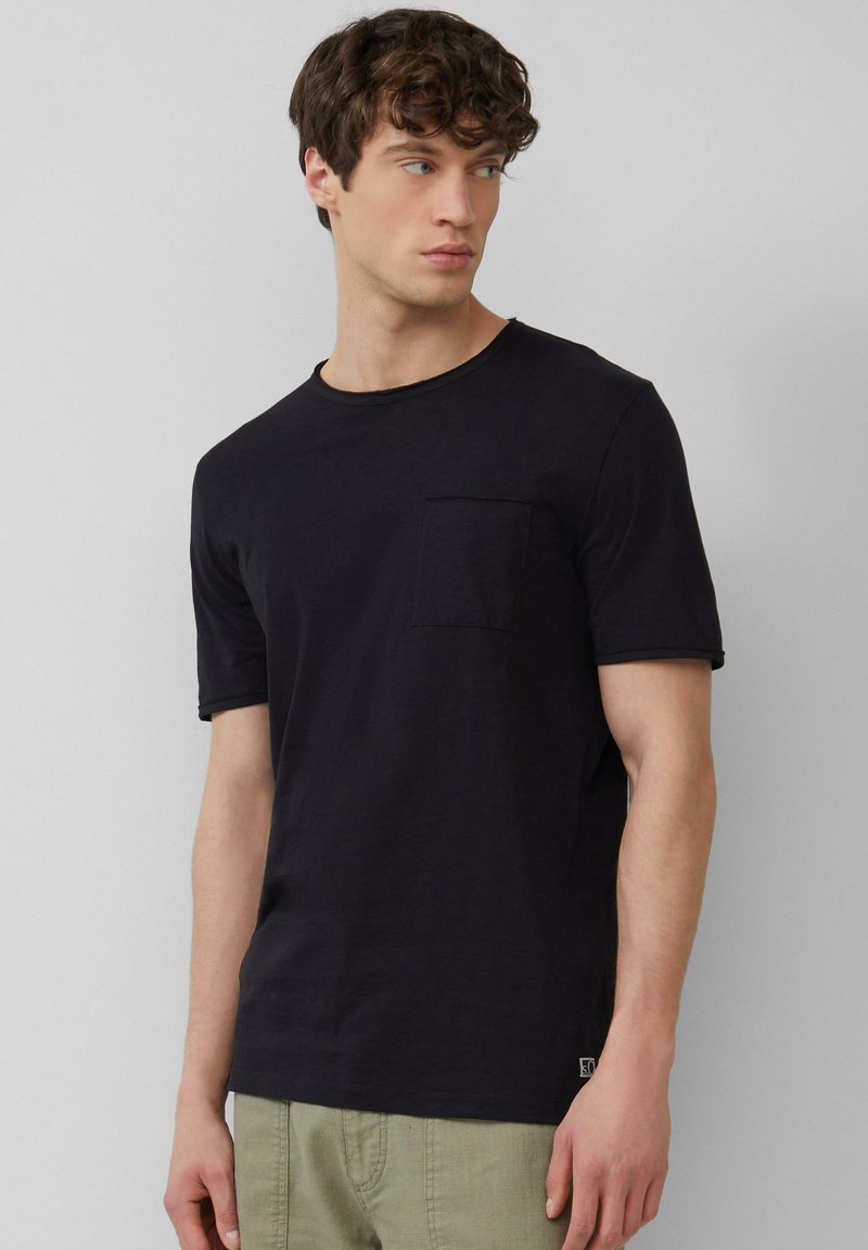 Zwarte T-shirt met ronde hals en korte mouwen, voorzien van een voorzak. Gemaakt van zachte stof met een gladde textuur en subtiele stikseldetails.