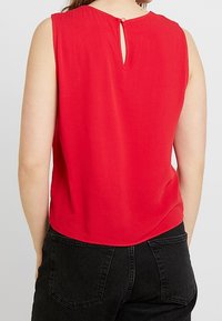 Top rosso senza maniche con orlo arrotondato e dettaglio a chiave sulla schiena fissato da un bottone. Tessuto morbido, design casual.