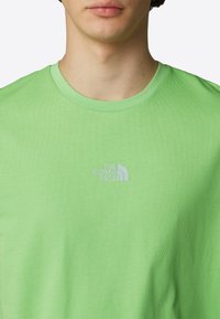Zelené bavlněné tričko s kulatým výstřihem a reflexním logem značky The North Face na hrudi. Hladká textura.