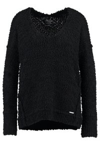Pull noir en tricot avec un col en V, des manches longues et une surface texturée et duveteuse. Présente une fente sur le côté et une petite étiquette de marque.