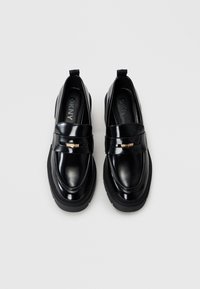 Μαύρες λαμπερές δερμάτινες loafers με διακοσμητική ταινία και χρυσές λεπτομέρειες, διαθέτοντας παχύ μαύρο πάτο και σχέδιο στρογγυλής μύτης.