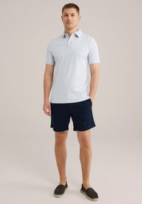 Polo bleu clair avec un motif texturé, manches courtes, patte de boutonnage à trois boutons, associé à un short navy et des chaussures noires à enfiler.