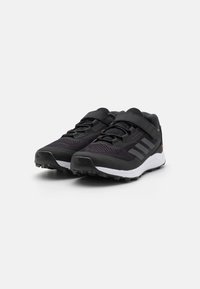 Baskets de sport noires avec une tige en mesh texturé, une bande Velcro et un design à trois bandes. Elles présentent une semelle intermédiaire blanche et une semelle extérieure robuste.