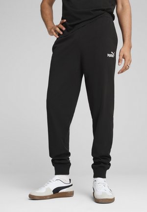 Schwarze Sportpants aus glattem Material, mit elastischem Bund, enganliegenden Bündchen und einem weißen Puma-Logo auf dem linken Oberschenkel.