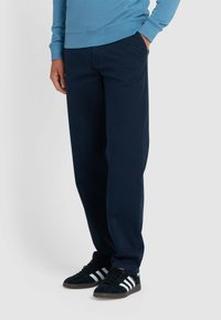 Marineblauwe broek in een ontspannen pasvorm, gemaakt van een gladde stof; gecombineerd met donkere sneakers met witte strepen.