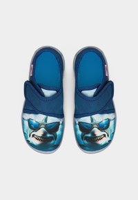 Chaussons bleus pour enfants avec des sangles réglables et des visages de requins portant des lunettes de soleil imprimés à l'avant.