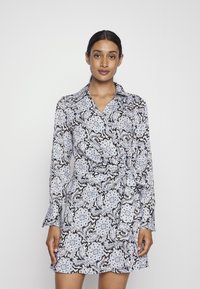 Vestido envolvente com padrão preto e branco, detalhes florais azuis, mangas longas e gola; o tecido parece suave e leve.