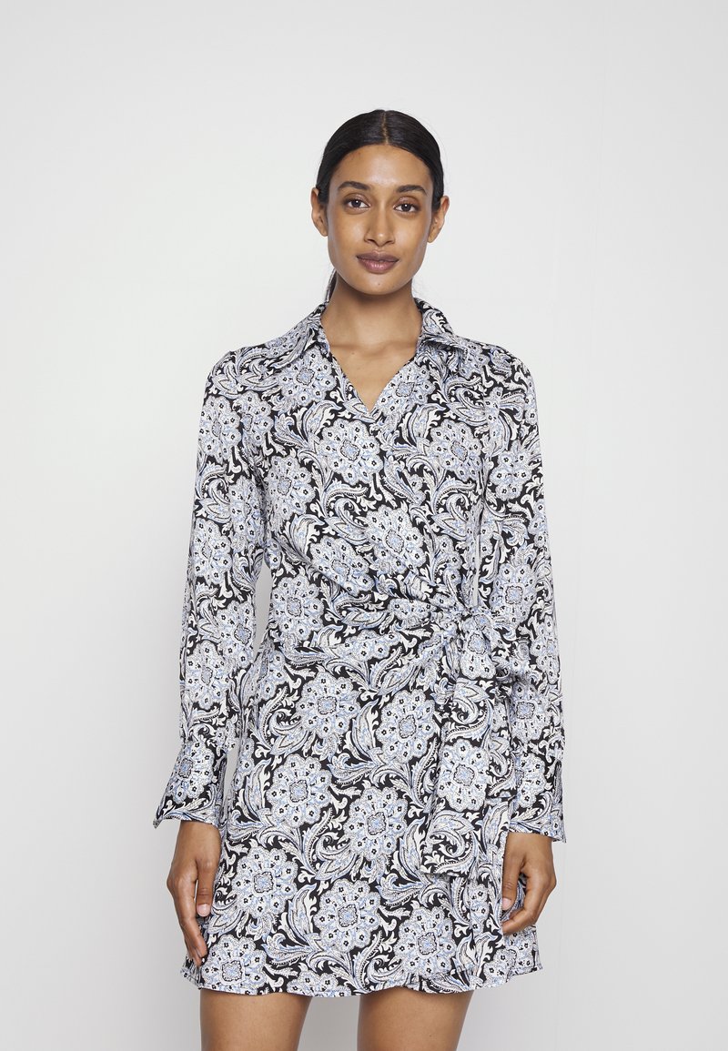 Vestido envolvente com padrão preto e branco, detalhes florais azuis, mangas longas e gola; o tecido parece suave e leve.