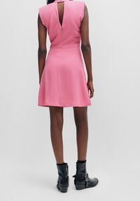 Rosa ärmelloses Kleid mit einem ausgestellten Rock, Rücken-Reißverschluss und Cut-out-Details. Getragen mit schwarzen Knöchelschuhen mit metallischen Akzenten.