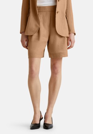 Pantalones cortos de lino color beige con un diseño de corte recto, que presentan un frente plisado y bolsillos laterales, combinados con zapatos de tacón negro tipo slingback.