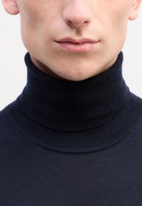 Tengeri turtleneck pulóver puha kötött anyagból, magas gallérral, sima felülettel és testhezálló kialakítással a nyak és a mellkas körül.