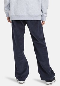 Marineblå kordfløjl bukser med brede ben, der har en blød tekstur og elastisk talje, sammen med sorte sneakers med hvide såler.