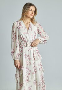 Abito floreale in tessuto leggero, con scollatura a V, maniche lunghe, orli a volant e vita con cintura, su una base bianca con fiori rosa.