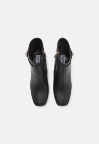 Paire de bottines en cuir noir avec fermetures éclair latérales dorées et bouts carrés, vues de dessus sur un fond blanc.