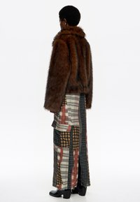 Chaqueta de piel sintética marrón con cuello alto, combinada con una falda maxi de múltiples patrones en diseños de cuadros y rayas. Botines negros.