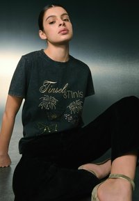 Czarny t-shirt ze złotym i cekinowym wzorem przedstawiającym kieliszki do martini i fajerwerki. Krótkie rękawy, okrągły dekolt, wykonany z bawełny.