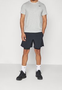 Camiseta corta de Nike de color gris, pantalones cortos deportivos negros, calcetas blancas y zapatillas deportivas negras. Tejido suave y ajuste relajado.