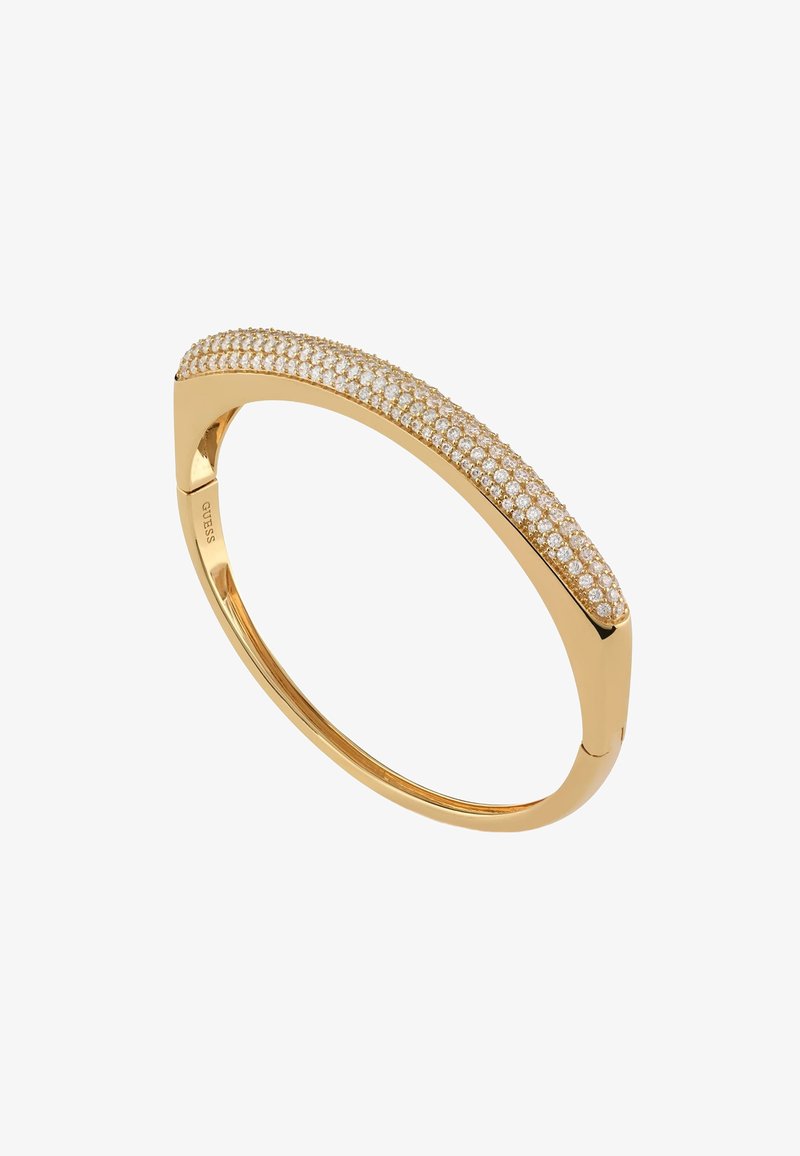 Bransoletka bangle w kolorze złotym, z zakrzywionym kształtem, ozdobiona przezroczystymi cyrkoniami wzdłuż górnej krawędzi, z gładkim, wypolerowanym wnętrzem.