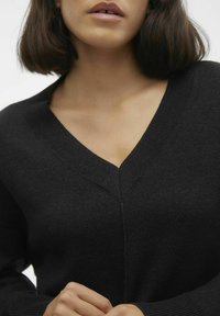 Maglione nero a scollo a V con collo e polsini a coste, maniche lunghe e una texture liscia. La caratteristica principale è il design profondo dello scollo a V.