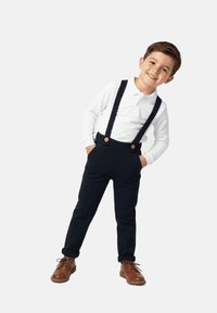 Biała koszulka polo z długim rękawem, ciemnoniebieskie spodnie z szelkami i guzikami oraz brązowe buty. Klasyczny strój dziecięcy, dopasowany fason.