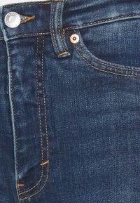 Jeans de ganga azul escuro com acessórios na cor cobre, costura dourada contrastante e uma textura suave. Apresenta um design clássico de cinco bolsos.