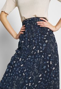 Kukkasilkkipettuhame tummansinisestä kankaasta, jossa on valkoisia ja vaaleansinisiä kuvioita. Hameessa on joustava vyötärö ja verkkomainen pinta.