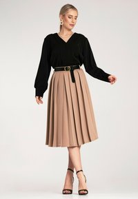 Czarna bluzka z długim rękawem i dekoltem w serek, zestawiona z beżową, plisowaną spódnicą midi i czarnym pasek. Czarne sandały na obcasie dopełniają stylizację.
