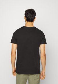 Camiseta de algodón negra con mangas cortas, cuello redondo y un diseño liso, que presenta un pequeño logo en la manga izquierda.