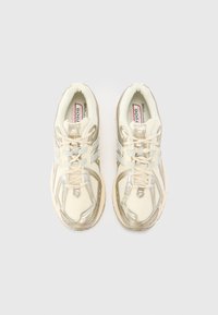 Beige athletic shoes with a textured mesh upper, silver accents, and a cushioned sole. Features New Balance logo and laces.