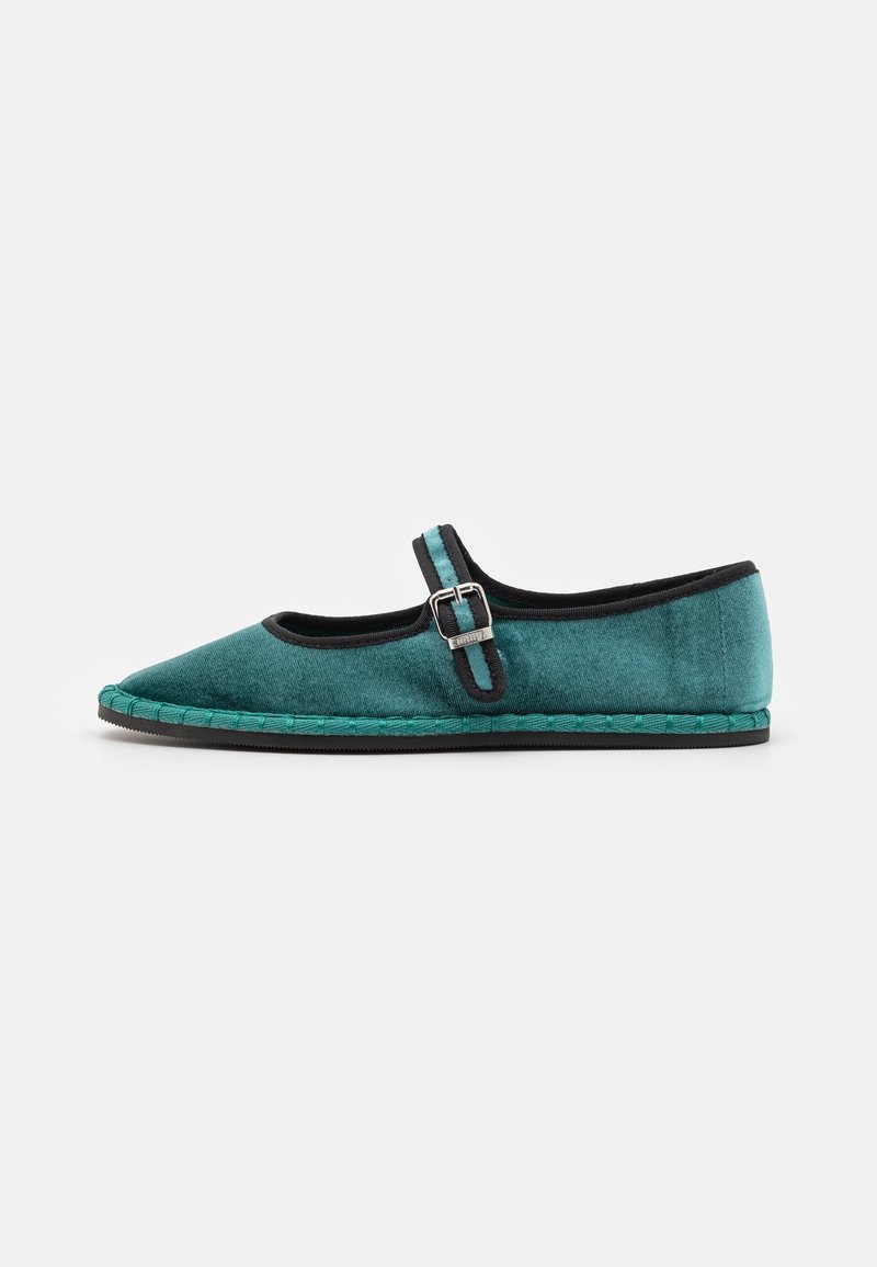 Chaussure Mary Jane en velours turquoise plat avec bordure noire, bride à boucle, détails tressés sur la semelle et semelle extérieure en caoutchouc noir sur fond uni.
