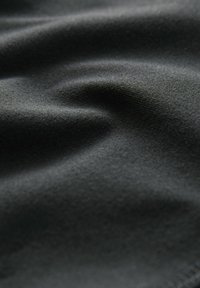 Crni materijal s glatkom teksturom, prikazuje suptilne nabore i mat finiš. Materijal izgleda lagano i rastezljivo.