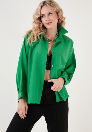 Green button-up blouse made of smooth fabric, featuring a relaxed fit, long sleeves with cuffs, and a pointed collar. Black lace top underneath.