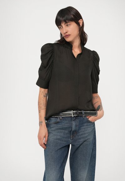 Mustast kangast lühikeste varrukatega pluus, millel on tekstuurse mustriga paelad, puhvvarrukad ja kraega kaelus, kombineeritud siniste teksapükste ja naelutatud vööd.