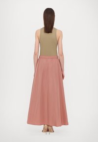 Gonna maxi leggera color rosa con vita elastica, abbinata a una canotta aderente color oliva, che mostra una superficie liscia e un design fluente.