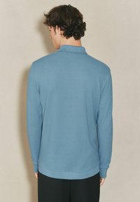 Polo a maniche lunghe in tessuto texture azzurro chiaro, con colletto, polsini a coste e orlo dritto. Vista posteriore mostrata.