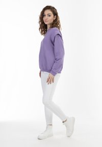 Felpa viola con spalle cadenti, polsini e orlo a costine, abbinata a jeans skinny bianchi e sneakers alte bianche.