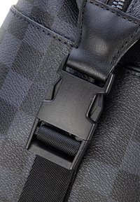 Czarny teksturowany materiał o połyskującym wykończeniu, z czarną plastikową klamrą i regulowanym paskiem, podkreślający trwałą konstrukcję.